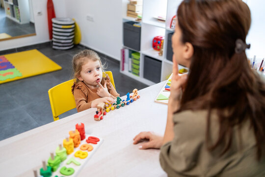 Speech therapist assisting a young girl with speech development, engaging in language lessons and communication therapy using educational toys in a school setting