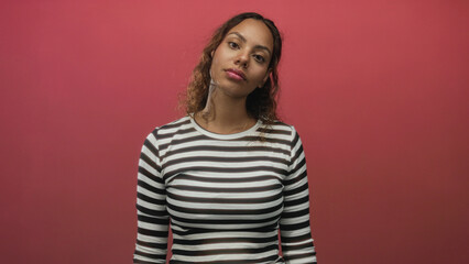 Fototapeta premium Woman facing camera with visible face and chest wearing striped shirt and slight smile in pink studio; quiet poised confidence.