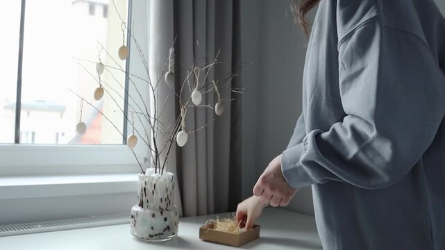 House decorating before Easter holidays: girl hanging small souvenir eggs on handmade Easter tree at home.