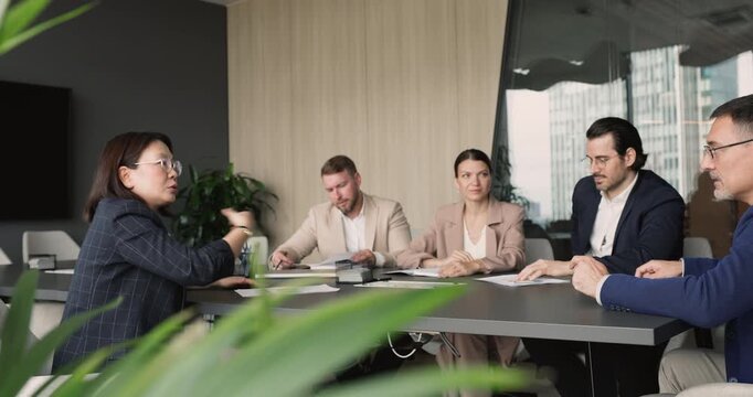 Diverse group of business people listening female leader, gather at conference table during formal corporate briefing, engage in negotiation or stakeholder discussion, consulting and executive meeting