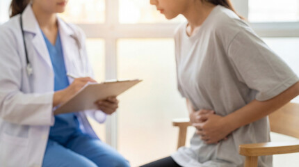 Fototapeta premium Blurred medical consultation scene featuring a doctor writing on a clipboard while a patient in a grey t-shirt holds her abdomen in pain. Concept for endometriosis diagnosis and women's healthcare.