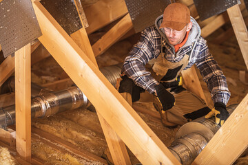 Fototapeta na wymiar Worker Installs Duct in Attic Space in Winter Time