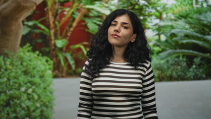 Naklejka premium Woman in striped top looks up, head tilted amid green foliage in a forest setting, relaxed posture and natural expression; quiet contemplation.