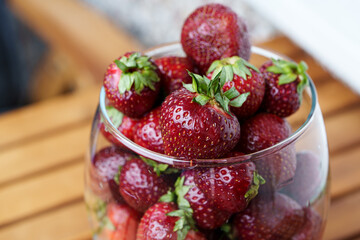 Garden strawberries in a glass goblet. Fresh strawberries with green stems placed in a transparent glass. Dark red berries with small shiny seeds on the surface. View from top to bottom.
