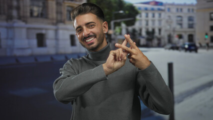 Young hispanic man showing hashtag sign with hands on urban street wearing grey sweater; social connection.