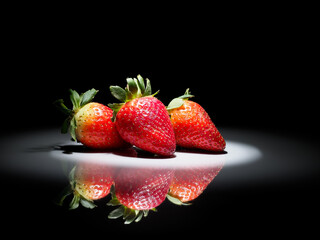 strawberries in a circle of white light on a black background with reflection in the shiny ground
