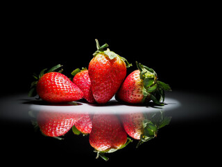 strawberries in a circle of white light on a black background with reflection in the shiny ground