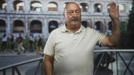Fototapeta premium Man waves hand at camera in front of an ancient stone building with arches and railing, tourists and street scene visible; nostalgia travel.
