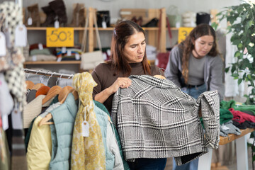 Fototapeta premium Selective Latina woman choosing some outwear for autumn-winter in clothing shop with large assortment