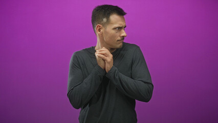 Fototapeta premium Hispanic young man with moustache looks right, hands clasped near chest, face and neck visible, wearing dark long sleeve shirt in studio; pensive doubt.