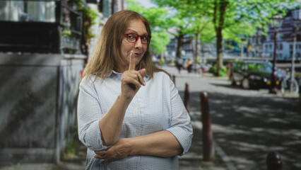 Fototapeta premium Woman points finger on street beside bicycle and parked cars, wearing glasses and casual shirt; friendly reminder.