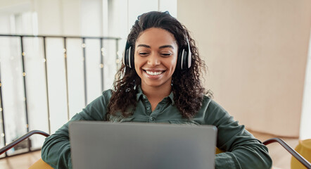 A woman with curly hair wears headphones and smiles while sitting at a laptop. She appears to be enjoying music or a video. Natural light fills the room as she engages with her device.