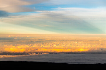 Fototapeta premium Sunset view from the summit of Mauna Kea on the Big Island of Hawaii, with volcanic slopes and clouds glowing in golden light.