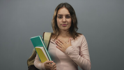 Fototapeta premium Young hispanic woman holding notebooks with hand on chest in neutral grey studio setting; gratitude study focus.