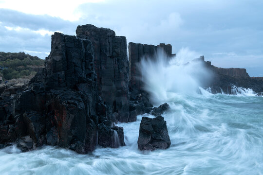 Powerful ocean waves crashing over dark basalt rocks at Bombo Quarry, Kiama, New South Wales, Australia. Dramatic coastal seascape with motion blur water.