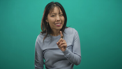Woman pointing index finger with rings toward camera in studio, wearing long sleeve sweater and hoop earring, teal backdrop  playful charm. © Krakenimages.com