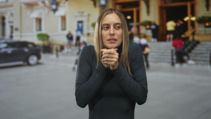 Fototapeta premium Young hispanic woman clapping hands near a building entrance on a busy city street with steps and parked car; determination resolve confidence.