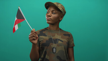 Young african american woman in camouflage uniform holds small kuwait flag with hand near chest in...