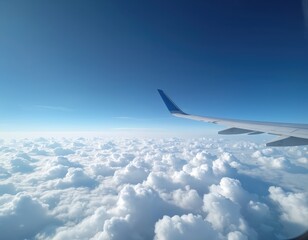 View from airplane window showing white clouds below vast blue sky. Airplane wing extends into frame, suggesting flight and travel above atmosphere.