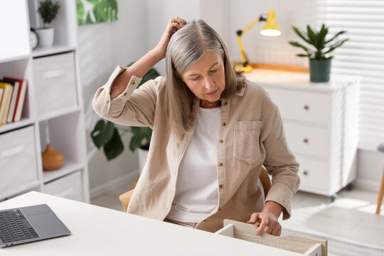 Amnesia. Senior woman trying to remember something at white table indoors