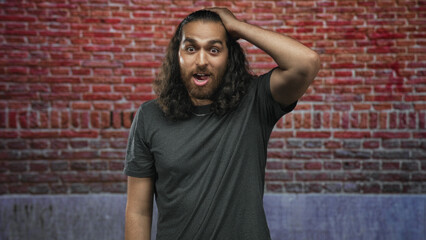 Obraz premium Man with hand on head against brick wall in a building, mouth open in a surprised gesture; surprise curiosity.