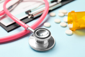 Stethoscope, clipboard and pills on light blue background, closeup