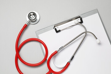 Stethoscope and clipboard on light grey background, top view
