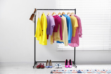 Different stylish clothes hanging on rack, bags and shoes indoors