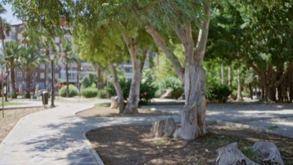 Obraz premium Park walkway with defocused trees, curved stone path and distant apartment buildings in soft bokeh background; background, copyspace, overlay, calm.