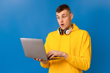 Emotional caucasian guy looking at laptop screen in shock, excited about win or success over blue...