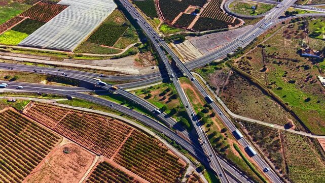 Vehicles travel along multiple lanes at a highway intersection, with farmland and crops visible in the surrounding areas during the day.