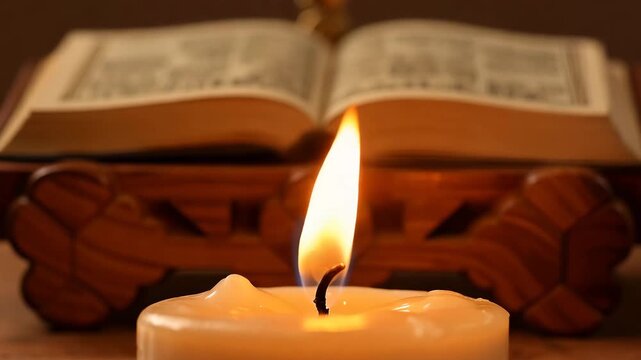 Close-up of burning candle flame with open Quran on wooden stand in background. Islamic religious concept for Ramadan and prayer