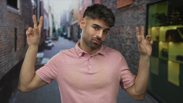 Hispanic man making air quotes gesture with fingers on narrow brick urban street in city; skepticism.