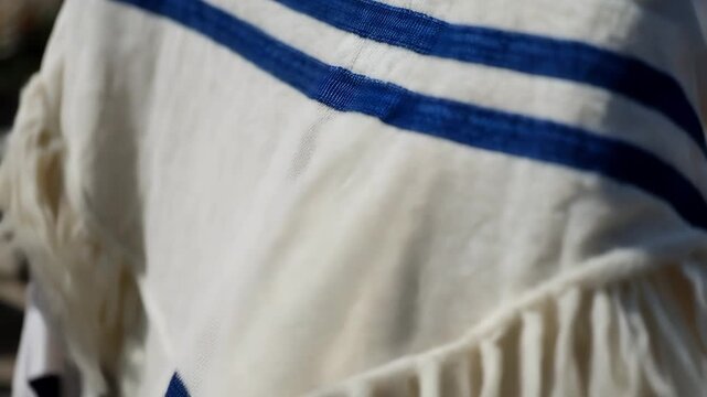 Jewish tallit prayer shawl with blue stripes and fringes. Close-up of traditional white religious cloth swaying in the sunlight. Judaism faith and ritual concept