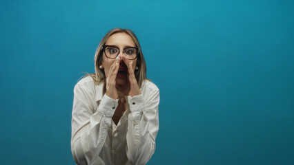 Woman wearing white shirt and glasses cupping hands around mouth calling out in teal studio; urgent announcement.