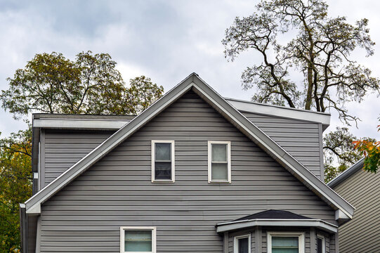 Suburban house with gray vinyl siding and white trim under a cloudy autumn sky in Boston, Massachusetts, USA
