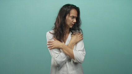 Obraz premium Woman hugging shoulders with crossed arms in studio wearing white blouse, tense expression and closed posture conveying self comfort; anxiety vulnerability.