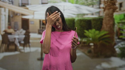 Fototapeta premium Young thai woman brunette holding a bamboo toothbrush and pressing hand to cheek for toothache in street cafe with umbrellas and tables; discomfort.