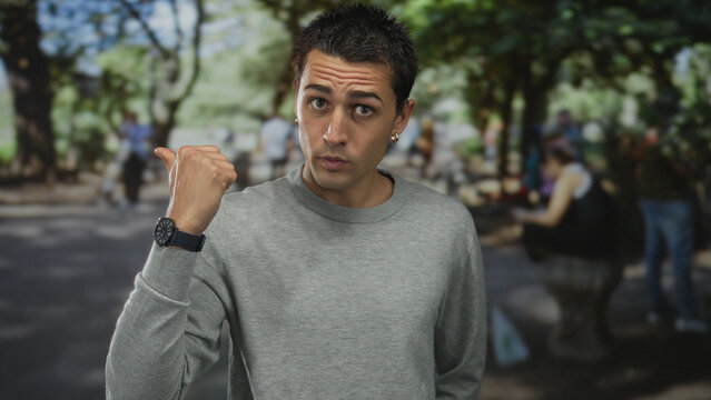 Man hand showing thumbs down gesture in street under trees during daylight outdoors; dismissal disapproval.