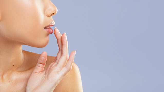 A woman is positioned sideways, gently touching her lips with one hand. The background is a solid color that highlights her profile.