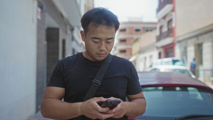 Man in black shirt holds smartphone and taps screen on sunny street; digital connectivity and concentration.