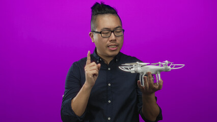 Man holding white quadcopter drone in his hand while pointing finger to its propeller in studio...