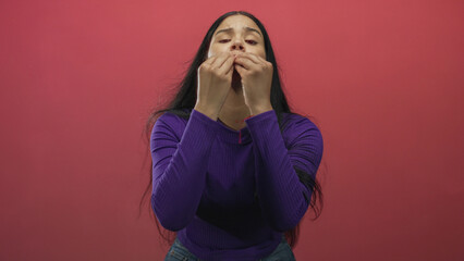 Young woman wearing purple sweater with outstretched hands pleading gesture in red studio;...