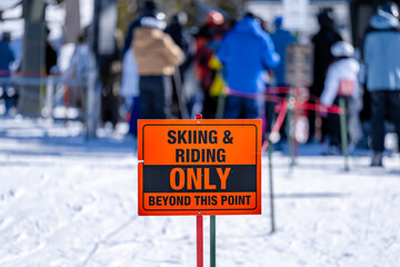 Skiing & Riding only beyond this point orange and black sign at ski lift. 
