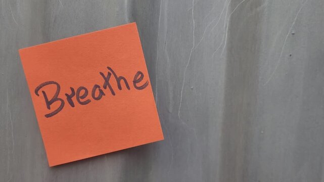 Orange sticky note with the word Breathe written in dark marker on a textured gray background