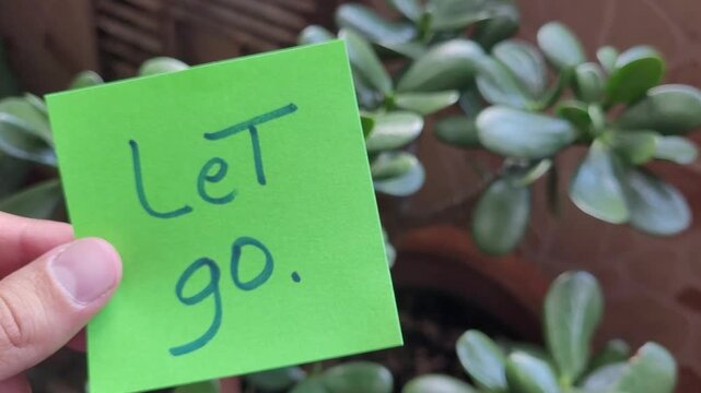 Hand holding a green sticky note with the words "Let go." written on it