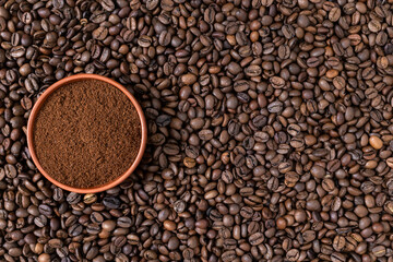 Fototapeta premium Top view of a small clay bowl filled with fresh ground coffee powder on a textured background of roasted beans. Flat lay composition. Concept of brewing, morning boost, specialty coffee, roastery