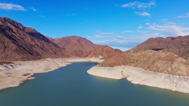 Aerial view of Orto Tokoy water reservoir surrounded by mountains in Kyrgyzstan. White embankments showing autumnal low water level in 2025.