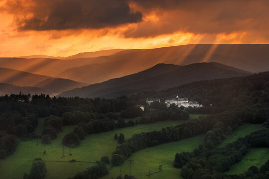 Dramatic sun rays breaking through dark, heavy clouds over the Priessnitz Spa resort in Jesenik, Czech Republic, creating a moody atmosphere.
