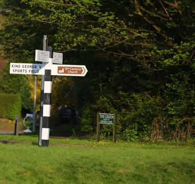 Traditional black and white fingerpost signpost on a village green in Sarratt, Hertfordshire pointing to a 12th century church